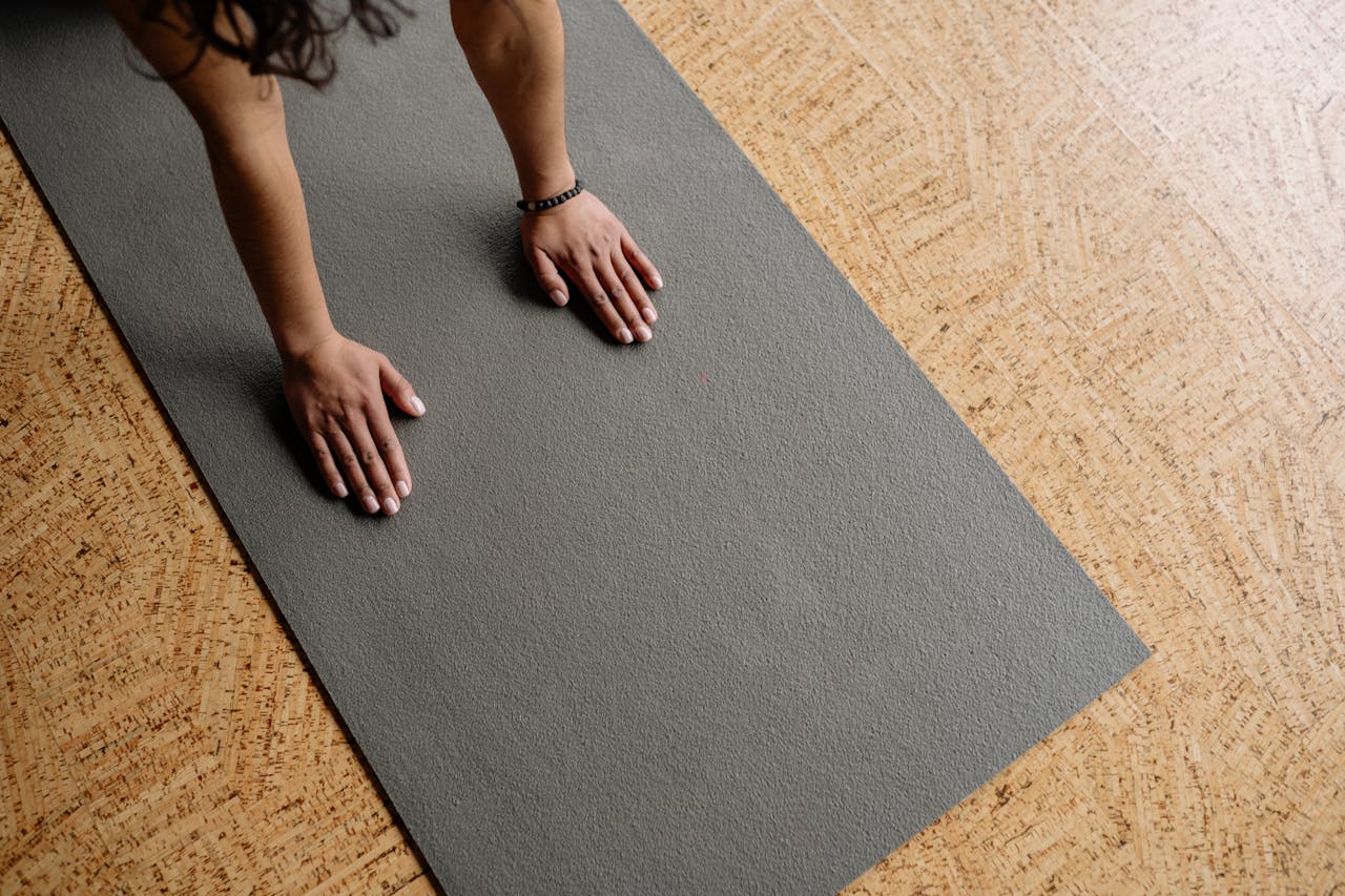 Close-up of hands on a grey yoga mat on a wooden floor, from above.